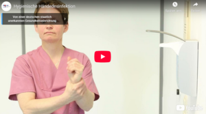 Person in rosa medizinischer Arbeitskleidung reibt die Hände aneinander und demonstriert Händehygiene vor einem Waschbecken