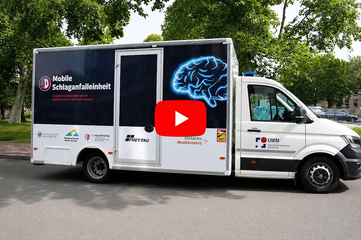 Mobile Schlaganfalleinheit der Universitätsmedizin Mannheim auf einer Straße unter Bäumen, mit leuchtendem Gehirnmotiv auf der Fahrzeugseite und rotem Play-Button in der Bildmitte.