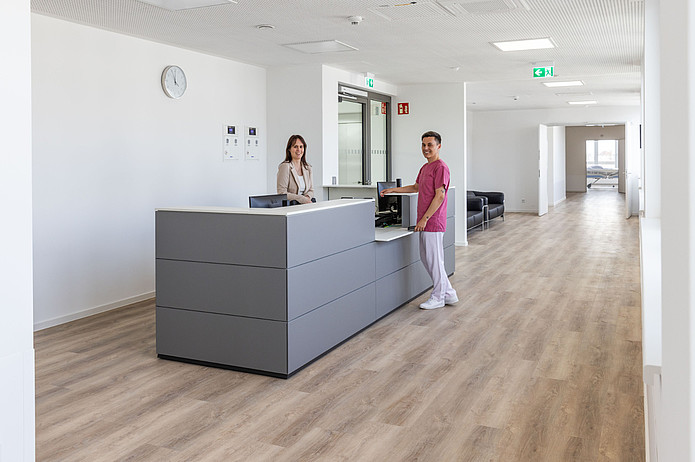Mitarbeiterin und Mitarbeiter stehen an einem Empfangstresen im Flur einer Krankenhausstation.