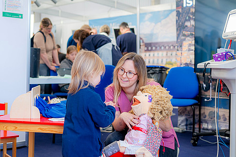 Blick auf das Mitmachangebot der Kinderchirurgie und Kindernotaufnahme. Eine junge Besucherin kann eine Puppe untersuchen.