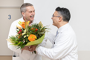 Zwei Mitarbeitende der UMM überreichen einen Blumenstrauß bei einer internen Ehrung.