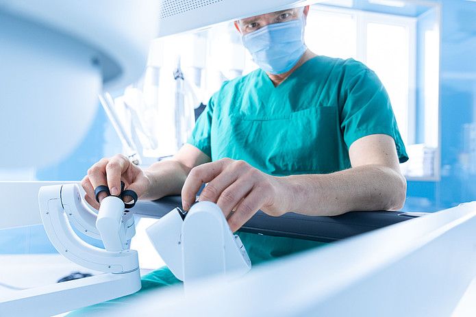 Chirurg sitzt an der Steuerkonsole eines robotergestützten Operationssystems und führt die Instrumente.