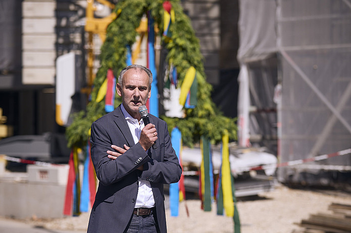 Architekt Martin Rieger hält Rede auf Richtfest: Mann im grauen Anzug spricht auf Baustelle.