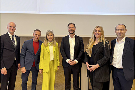 Sechs Personen in Businesskleidung stehen nebeneinander vor einer hellen Wand