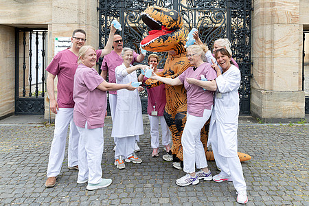 Mehrere Mitarbeitende und ein Dino stehen im Freien zusammen