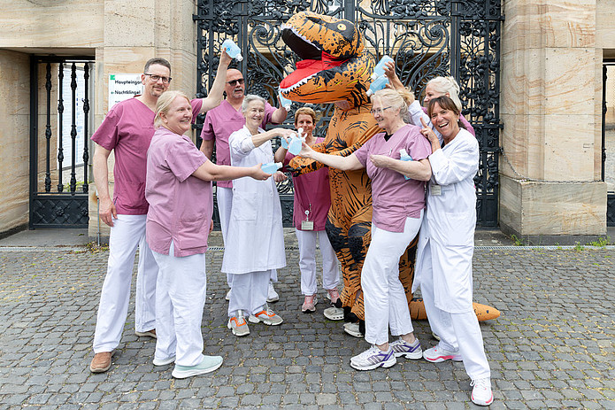 Mehrere Mitarbeitende und ein Dino stehen im Freien zusammen