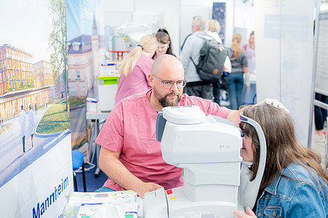 Blick auf das Mitmachangebot der Augenklinik mit einem Mitarbeiter und einer Besucherin. Mainmarkt Mannheim 2025. Besuch des Messestands des Universitätsklinikum Mannheim.