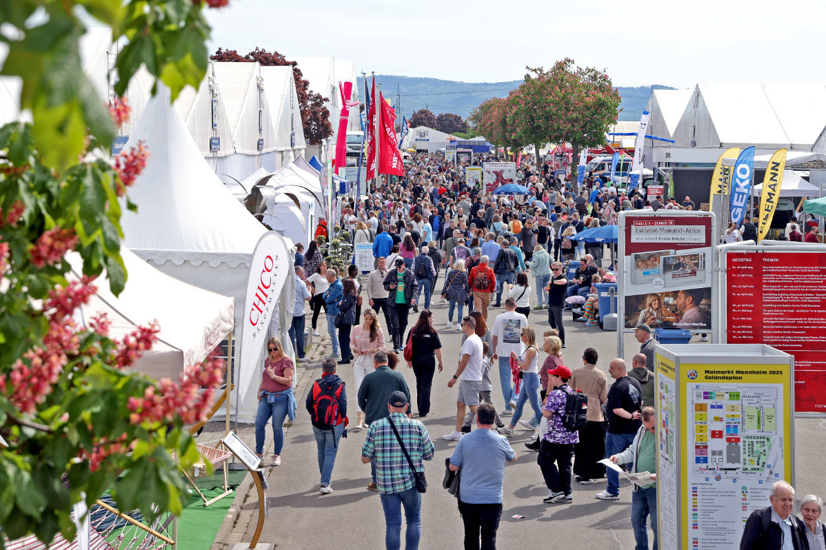 Menschenmenge auf einem Freiluftmarkt mit weißen Zelten, Fahnen und Informationsständen