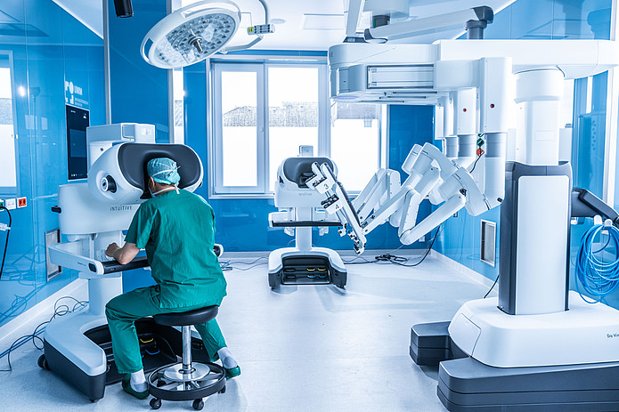 Chirurg sitzt an der Konsole eines robotergestützten Operationssystems im OP-Saal.