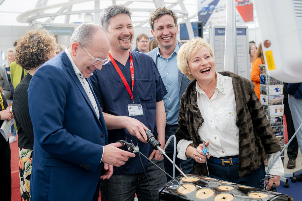 Gruppe von Personen an einem Messestand, zwei halten chirurgische Instrumente über eine schwarze Platte mit runden Aussparungen