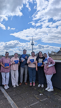 Gruppe von Mitarbeitenden steht im Freien zusammen und hält Informationsmaterial in den Händen.