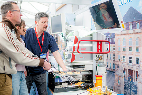 Ein Mitarbeiter und Besucher beim Mitmachangebots an dem man spielerisch mit Operationsbesteck hantiert.
