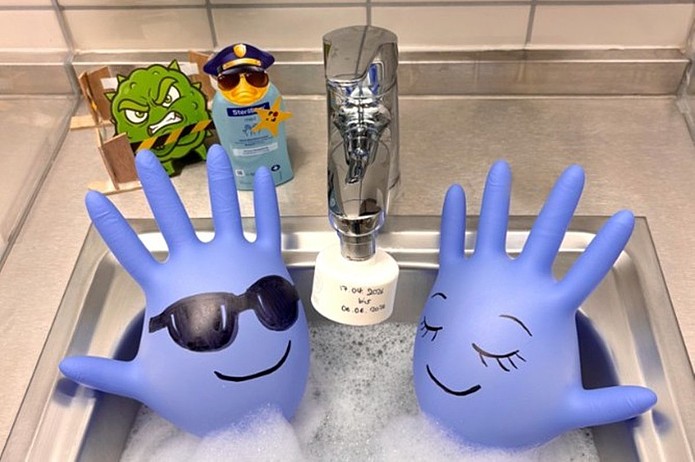 Zwei blau gestaltete Figuren in Form von Händen stehen mit Dekorationselementen am Waschbecken