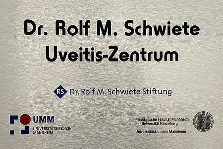 Das Bild zeigt das metallene Schild des Dr. Rolf M. Schwiete Uveitis-Zentrums 