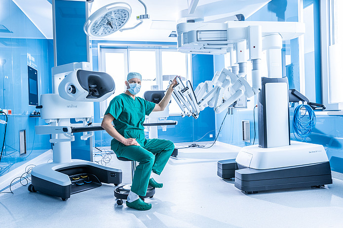 Chirurg sitzt im Operationssaal neben einem robotergestützten Operationssystem.