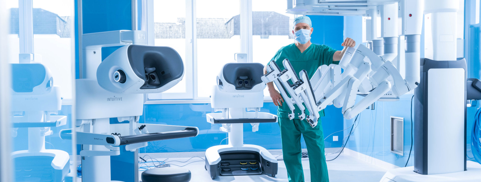 Chirurg im OP-Saal neben einem robotergestützten Operationssystem und weiteren medizinischen Geräten.