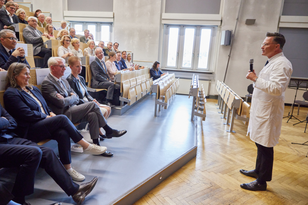 Mann in weißem Kittel spricht vor aufmerksamen Publikum