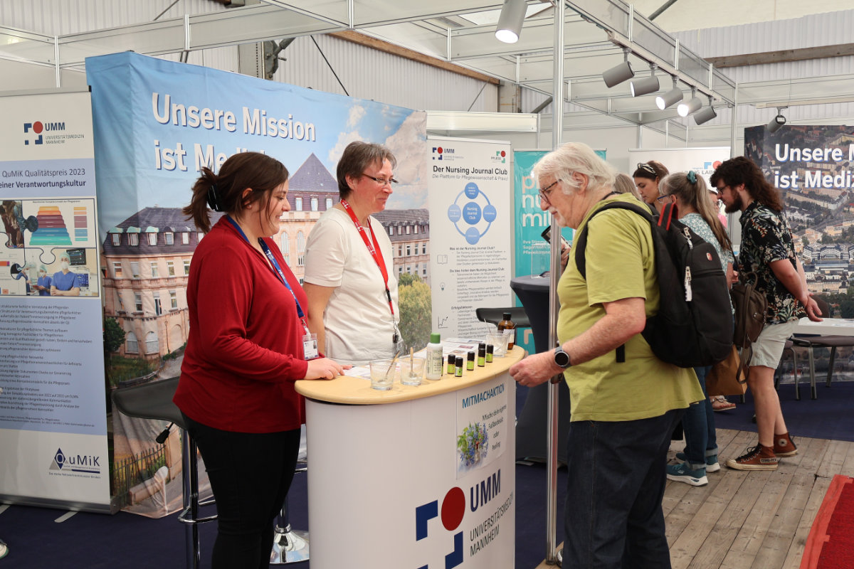 Mehrere Personen stehen an einem Messestand mit Bannern und Informationsmaterialien in einer Halle