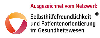 Logo mit farbigem, kreisförmigem Symbol in Orange-, Rot- und Gelbtönen links. Rechts daneben der Text: ‚Ausgezeichnet vom Netzwerk Selbsthilfefreundlichkeit und Patientenorientierung im Gesundheitswesen‘
